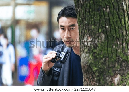 A man hiding in a tree and keeping a lookout with binoculars in the city. Royalty-Free Stock Photo #2291105847
