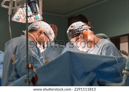 Surgeon face in operating room, stressful operation, surgeon performs operation in modern operating room with activity life support devices and light lamps, life saving, inoperable sarcoma. Royalty-Free Stock Photo #2291111813