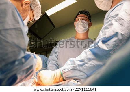 Surgeon face in operating room, stressful operation, surgeon performs operation in modern operating room with activity life support devices and light lamps, life saving, inoperable sarcoma. Royalty-Free Stock Photo #2291111841