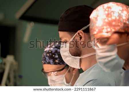 Surgeon face in operating room, stressful operation, surgeon performs operation in modern operating room with activity life support devices and light lamps, life saving, inoperable sarcoma. Royalty-Free Stock Photo #2291111867