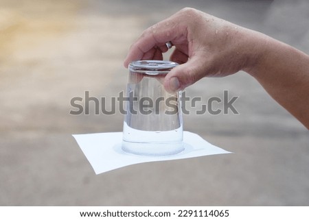 Closeup hand hold and turn  a glass of water over down. covered the glass with paper. Concept,  science experiment about air and liquid pressure. Easy science subject activity, education.             