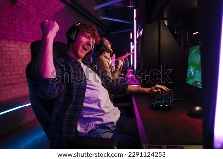 Team of professional gamers wearing headphones celebrating victory while playing online video game on tournament in modern cybersport club