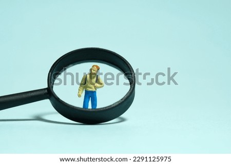 Miniature people toy figure photography. Children curiosity concept. A boy kindergarten student standing with black magnifier glass. Isolated on blue background. Image photo