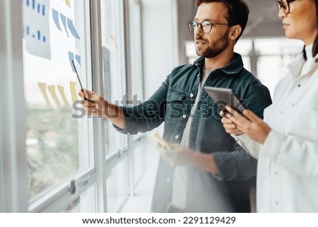 Creative business people brainstorming with sticky notes in an office. Business professionals standing next to a window and discussing their ideas. Royalty-Free Stock Photo #2291129429