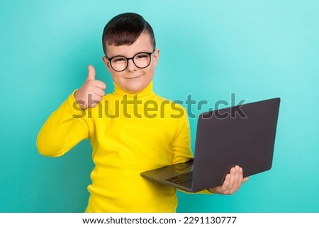 Photo of positive primary school boy student use netbook advertise with thumb up symbol isolated teal color background