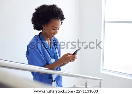Female Doctor Or Nurse Browsing On Mobile Phone On Stairs In Hospital