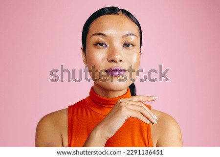 Woman looking at the camera while wearing a bold lip primer, giving her a striking look. Portrait of a woman in her 20s standing in a studio, expressing confidence and assurance in her appearance. Royalty-Free Stock Photo #2291136451