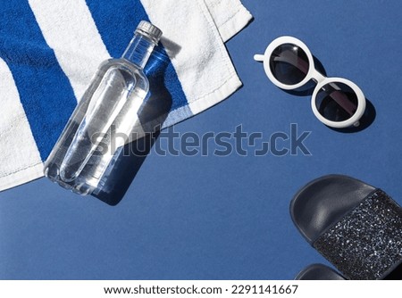 Summer vacation beach concept frame with retro sunglasses, striped towel and bottle of water on the blue background. Copy space