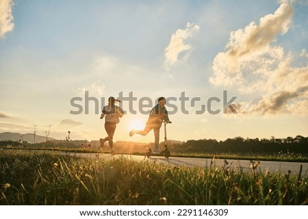 Happy family, mother and son go in sports outdoors. Boy rides scooter, mom runs on sunny day. Silhouette family at sunset. Health care, authenticity, sense of balance and calmness.