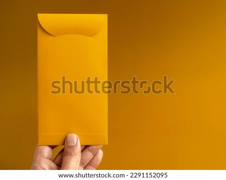 Hand holding a gold envelope, vertical style, isolated on yellow background with copy space. Hongbao packet for lucky money gift in Chinese lunar, new year on January month, exclusive packet. Royalty-Free Stock Photo #2291152095