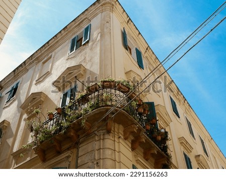 Rounded corner of the vintage buildings with metallic balcony decorated with house plants in Alghero, Sardinia, Italy.