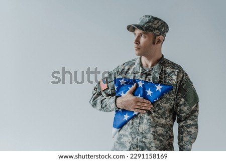 good looking American soldier in military uniform holding folded flag of United States during memorial day isolated on grey