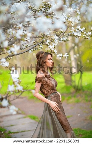 Spring Beautiful romantic girl in fashion  lace dress standing in blooming garden. Dreaming young model between magnolia trees.