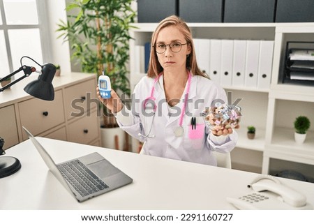 Young blonde doctor woman holding glucometer and sweets skeptic and nervous, frowning upset because of problem. negative person. 