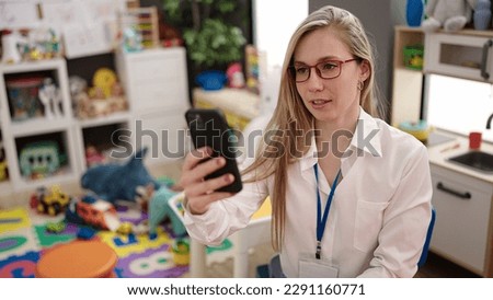 Young blonde woman preschool teacher having video call at kindergarten