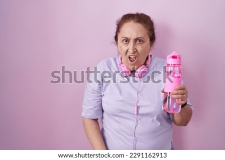 Senior woman wearing sportswear and headphones in shock face, looking skeptical and sarcastic, surprised with open mouth 