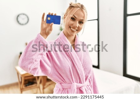Young caucasian woman wearing bathrobe holding credit card at beauty salon