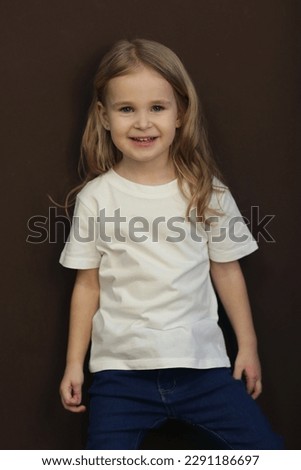 cute blond little girl in white t-shirt and jeans close up photo on dark brown background