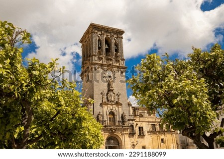 The bell tower of the Basilica of Santa Maria against the backdrop of blossoming orange trees and the sky in the city of Arcos de la Frontera, Andalusia, Spain Royalty-Free Stock Photo #2291188099