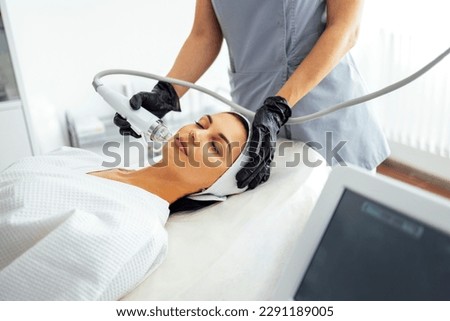 Microneedle RF lifting procedure. Hardware cosmetology. Beautician conducts a facial rejuvenation procedure for a brunette woman Royalty-Free Stock Photo #2291189005