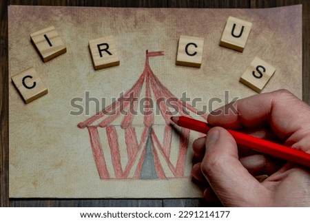 A male hand is coloring a drawing representing a circus tent with a red pencil