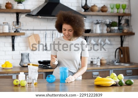 Young sporty african american woman pouring protein powder into a cup to make replacement food meal. Woman makes a protein cocktail in the kitchen at home. Functional Power, Sports Power Royalty-Free Stock Photo #2291222839