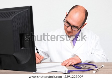 A bald caucasian doctor with eyeglasses wearing a white coat signing a health report over his office wooden table.
