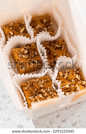 Packaging homemade pumpkin spice fudge with pecans into a white paper gift box.