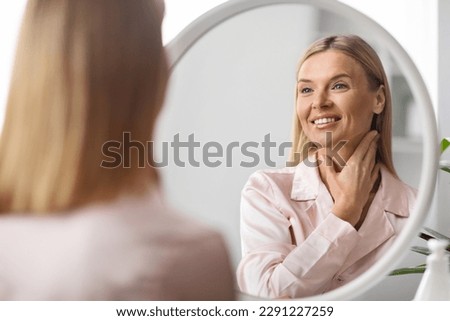 Beautiful Middle Aged Woman Looking At Mirror And Touching Her Soft Skin On Neck, Attractive Mature Lady Smiling To Reflection, Enjoying Anti-Aging Skincare Routine At Home, Selective Focus Royalty-Free Stock Photo #2291227259
