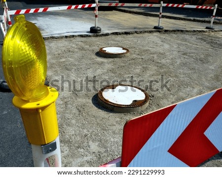 asphalt drive surface repair. exposed concrete base. manhole covers. road construction work. steel and concrete manhole covers. road hazard. red and white wood barrier and detour arrow sign.