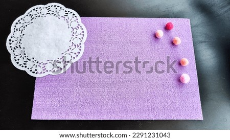 Top view of lilac or purple sheet of velvet paper, white a carved napkin and color ball. Abstract frame, background and texture with copy space. Empty rectangle with round paper napkin on black colour