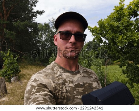 Ukrainian army man in sunglasses and in cap with drone smart controller in wild nature background. UAV operating. 
