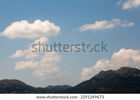 White clouds above the green hills on a sunny day, blue sky. Horizontal shot with empty copy space for text.