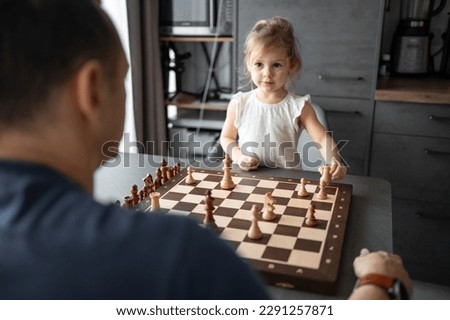 Father teaching his little daughter to play chess at the table in home kitchen. The concept early childhood development and education. Family leisure, communication and recreation. High quality photo