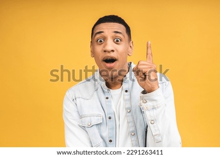 Portrait of happy young african american shocked amazed man in casual smiling, pointing up with fingers, isolated over yellow background.