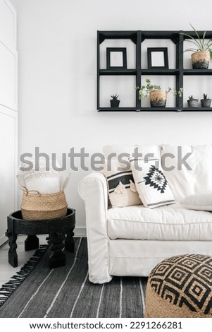 detail in lounge room with bohemian interior, comfort sofa and cushions with ethnic pattern, wicker basket on side table, wooden shelf with plants on wall and pouf on floor rug Royalty-Free Stock Photo #2291266281