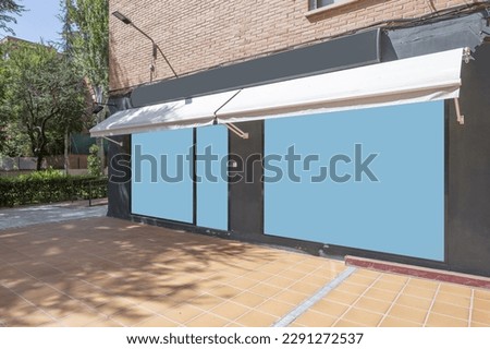 Gray facade of a commercial premises with awnings in the basement of a building with excess trees