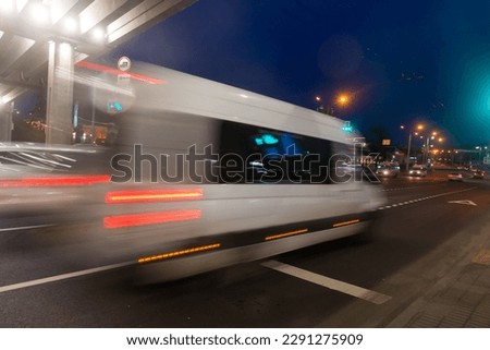 A blurred minibus moves under an overpass through the city in the evening 