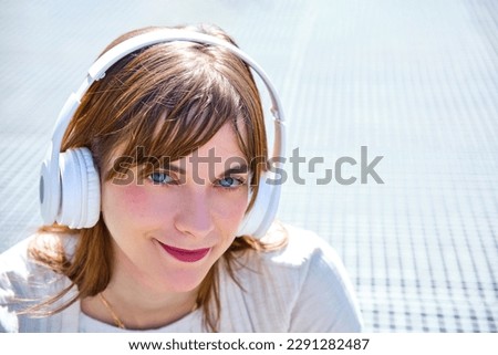 portrait of very pretty redhead blue eyes young girl wearing headphones listening to music looking at camera
