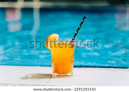 Tropical sparkling cocktail by the pool. The picture of glass with orange lemonade fruit cocktail standing near the poolside. Summer alcohol free drink by the hotel pool. Hello summer holiday vacation