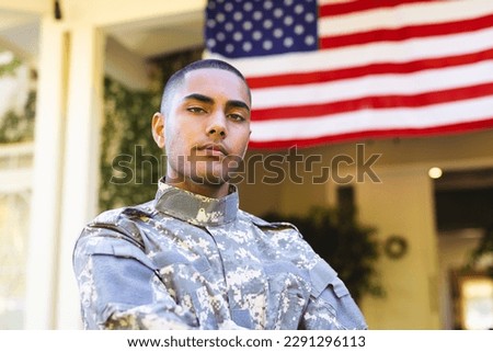 Portrait of biracial male american soldier wearing military uniform standing outside the house. American flag, patriotism and military service.