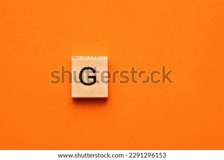 Alphabet letter G on wooden square tile - Orange foamy background Royalty-Free Stock Photo #2291296153