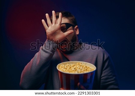 A man is in a dark room with neon lighting, watching a movie with 3D glasses and popcorn. High quality photo