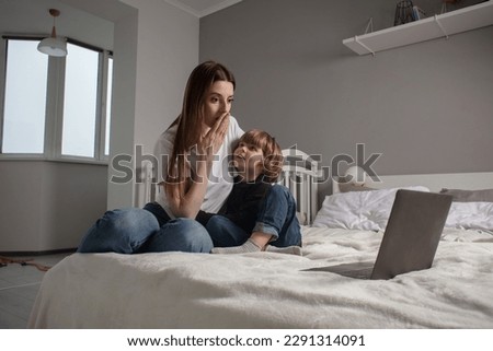 Happy mother with her little son enjoying in online shopping or working from home. Business from distance and virtual communication.
Mom and baby watch cartoons or play game on laptop on the bed.
