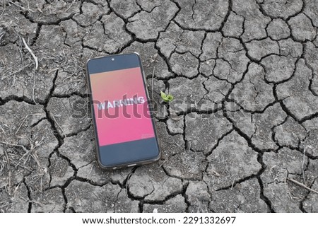 
A phone with a warning screen is on a cracked floor. Drought and climate crisis.