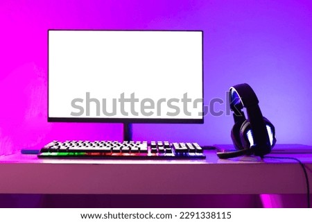A gamer's computer and headphones prepared for a new online game, illuminated with colored LED lights. Royalty-Free Stock Photo #2291338115