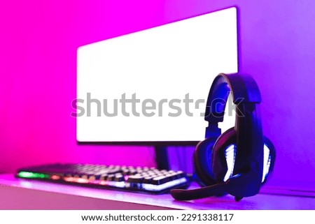 Wireless headphones next to a gaming computer, with LED lighting. Royalty-Free Stock Photo #2291338117