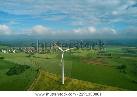 One wind turbine in the center of the picture on an agricultural field. Narrow road leading to a village on the swabian alb in germany. Blue sky with storm-like clouds. Aerial view.