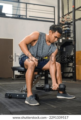 Asian young muscular fit strong body sporty athletic male fitness model in workout sleeveless sportswear holding lifting metal dumbbell weight training arms exercise at  gym Royalty-Free Stock Photo #2291339517