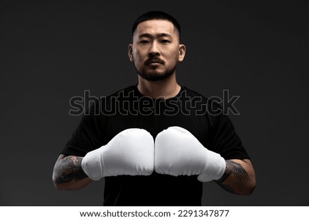 Dramatic portrait of handsome confident asian man, boxer wearing white boxing gloves, looking at camera isolated on black background. Sport, motivation concept 